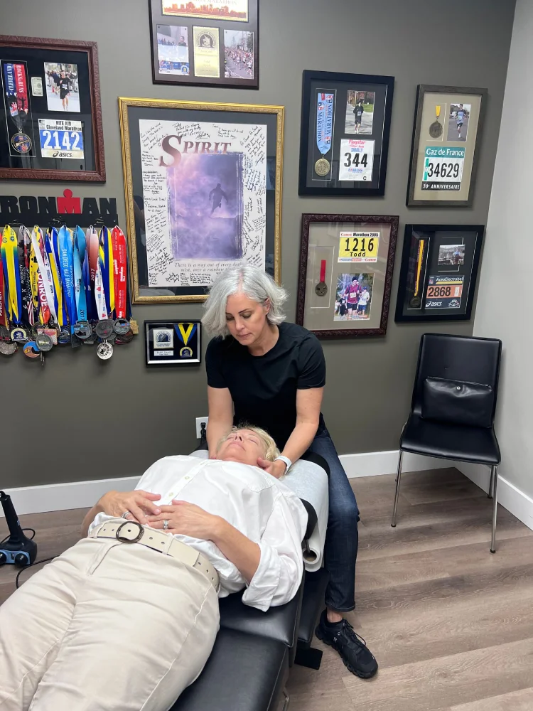 Female chiropractor assesses neck of female patient while she lays on treatment table