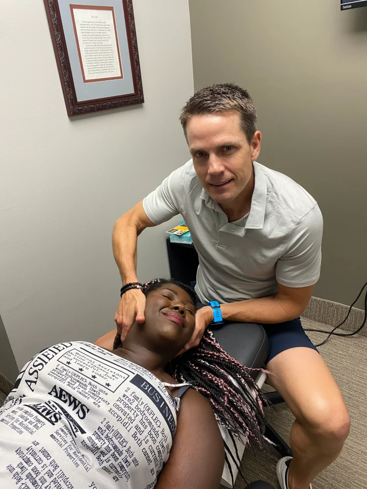 Male chiropractor smiles as he adjusts neck of female patient laying on treatment table